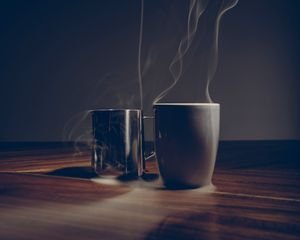 Company? Two steaming coffee mugs on a wooden table create a cozy, warm ambiance.